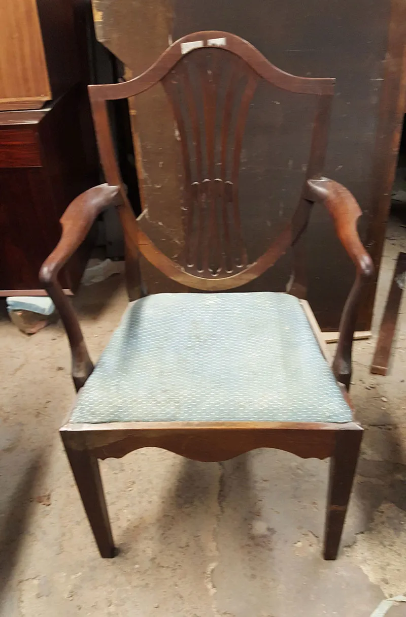 A shield-back dining chair in the workshop before restoration, its seat worn