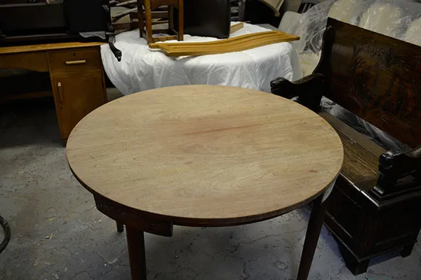 A round dining table in the workshop before restoration, its top faded and marked